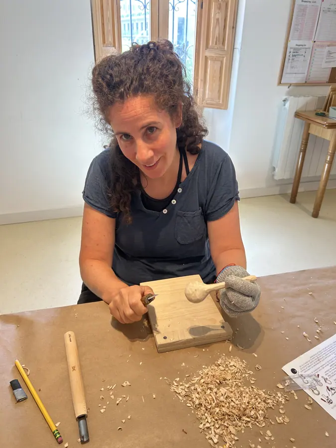 a participant carving a wooden spoon, shavings gathering on the bench