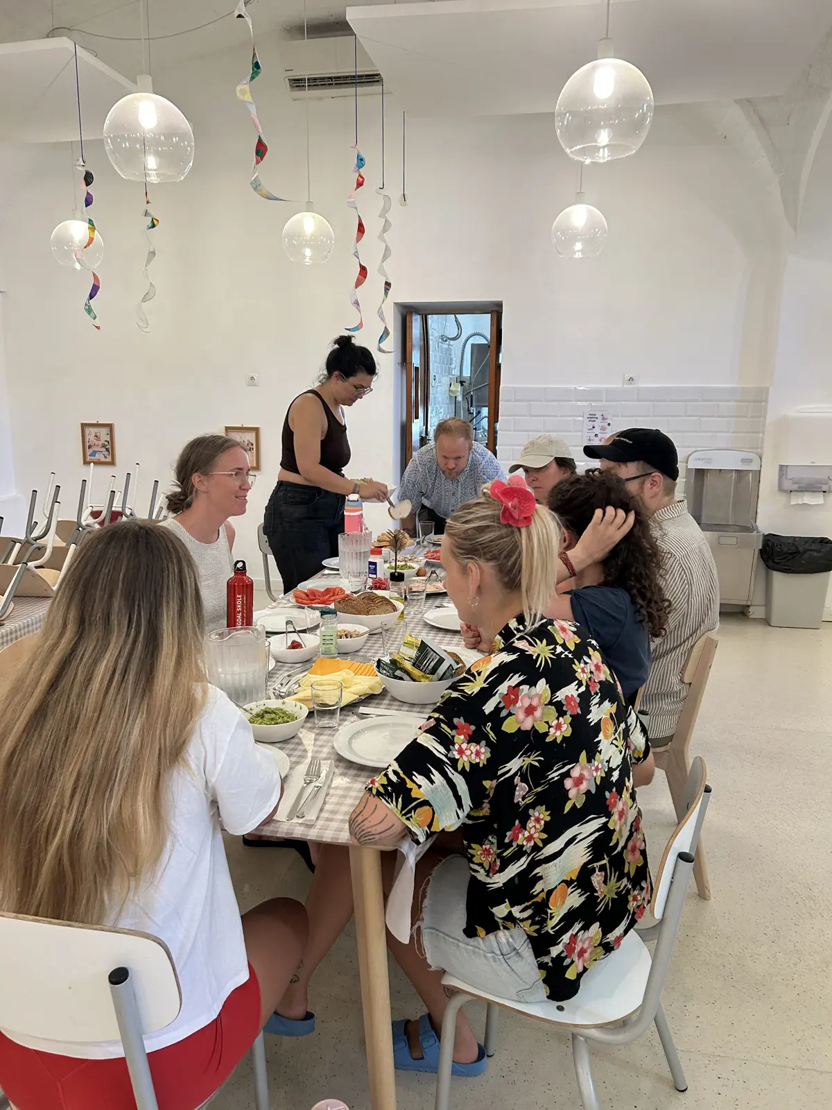 the cohort sharing a long lunch beneath paper decorations